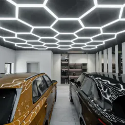 Nowoczesny salon samochodowy z dwoma samochodami: złotym i czarnym, podświetlony heksagonalnym oświetleniem sufitowym i minimalistycznymi białymi panelami ściennymi.