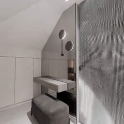 Adam Jasek Design Studio - Nowoczesna, monochromatyczna łazienka z toaletką z szufladami i lustrem pod skosem, oświetlona okrągłymi lampami ściennymi, z siedziskiem z tkaniny obok kabiny prysznicowej z metalową siatką.