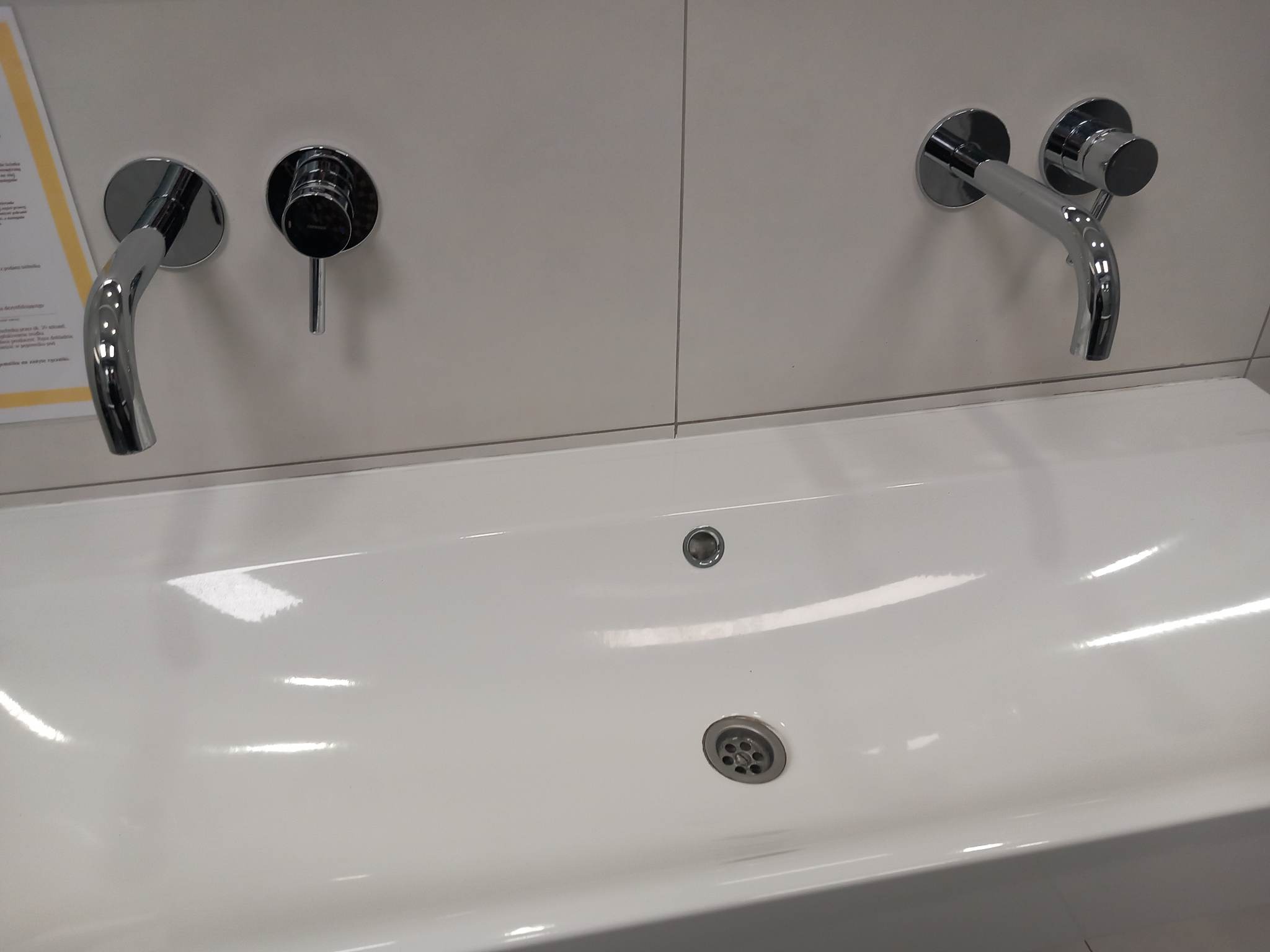 Biała umywalka z dwoma chromowanymi kranami ściennymi, widok z góry, minimalistyczny design łazienki.