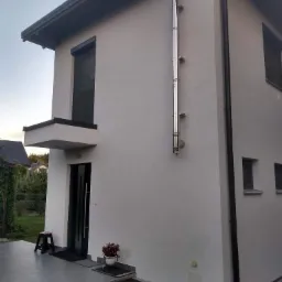 Nowoczesny dom jednorodzinny z białą elewacją, czarnymi detalami okien i dachu oraz zewnętrznym, metalowym kominem.