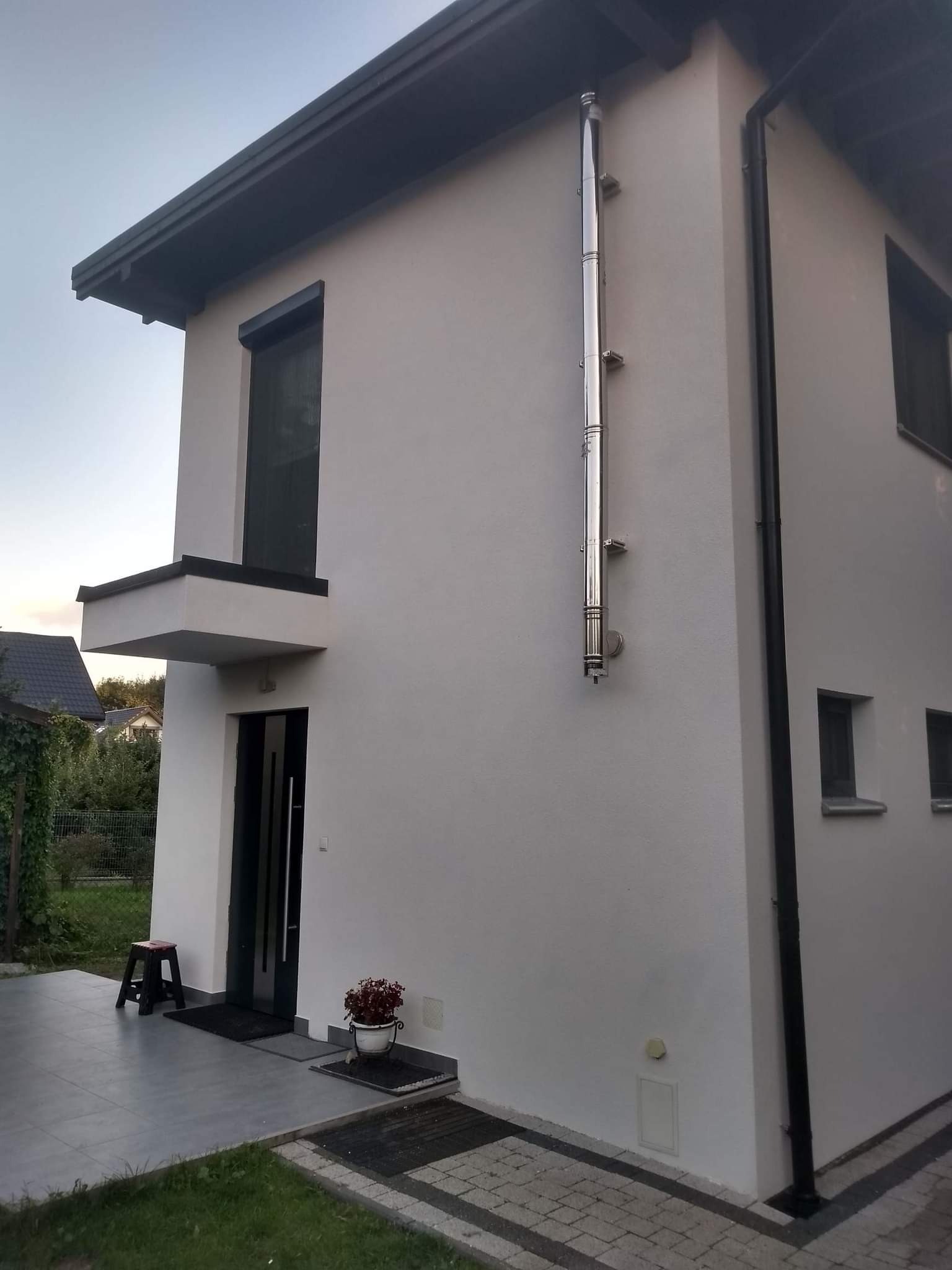 Nowoczesny dom jednorodzinny z białą elewacją, czarnymi detalami okien i dachu oraz zewnętrznym, metalowym kominem.