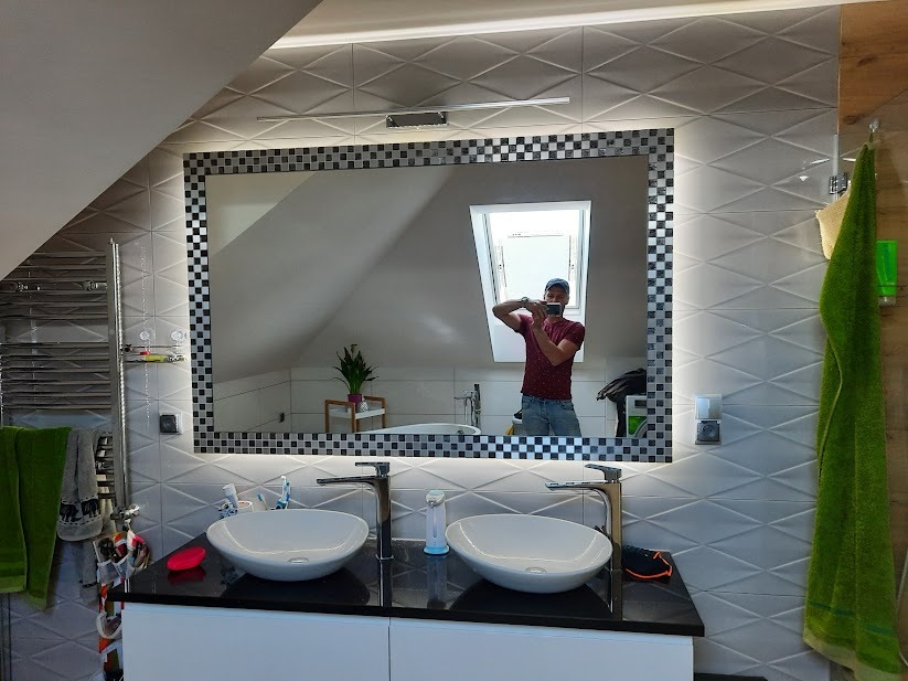 Nowoczesna łazienka na poddaszu z dwoma umywalkami nablatowymi, lustrem z podświetleniem LED i ramą w szachownicę, oraz widocznym odbiciem fotografa robiącego zdjęcie.