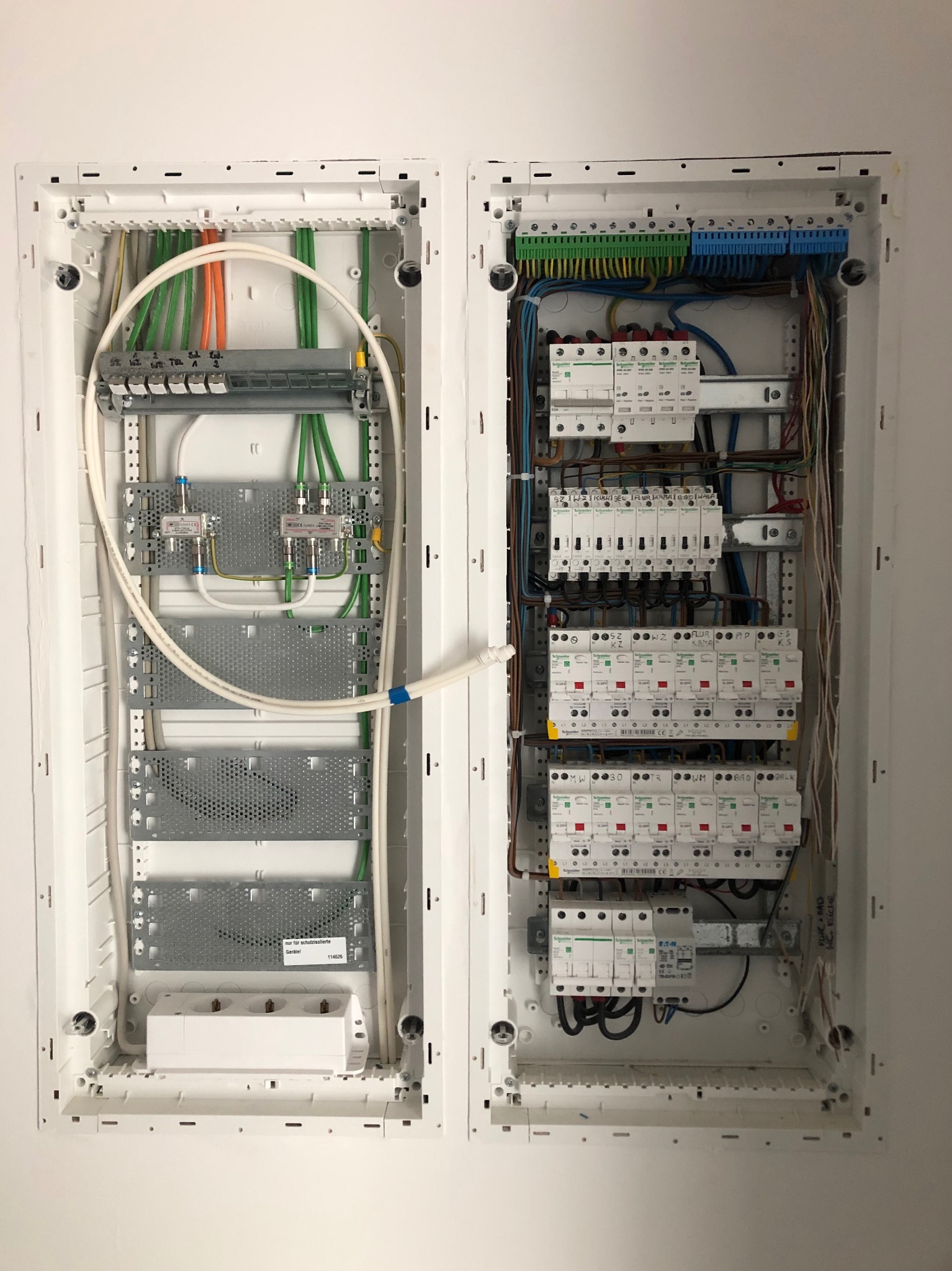 Dwa rozdzielne panele elektryczne zamontowane w ścianie, jeden z bezpiecznikami i okablowaniem, drugi z elementami instalacji antenowej i gniazdkami, widoczne przewody i listwy zaciskowe.