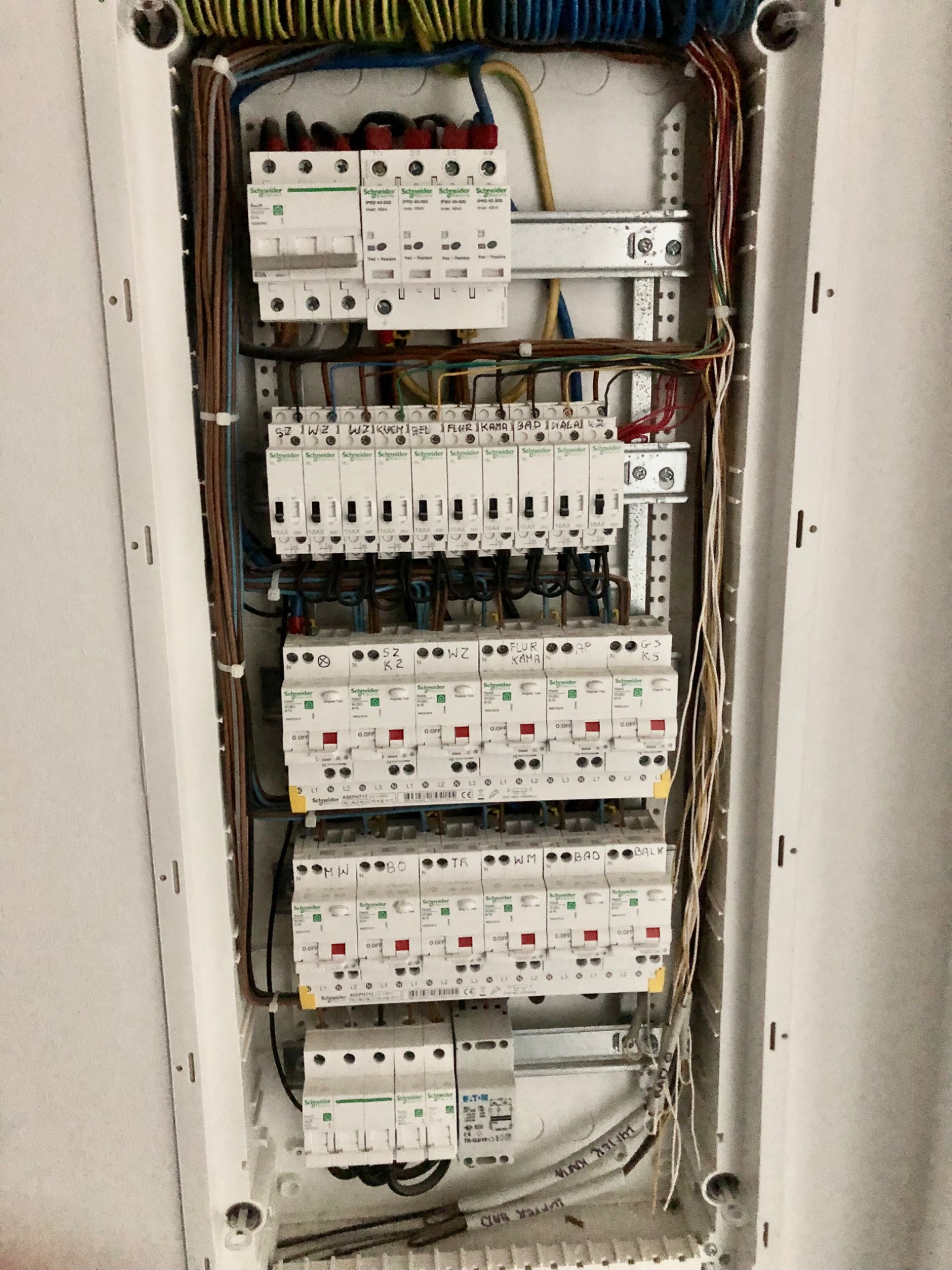 Rozdzielnica elektryczna z zainstalowanymi bezpiecznikami i przewodami, widoczne oznaczenia obwodów i elementy montażowe na szynie DIN.