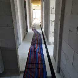 Instalacja rur ogrzewania podłogowego w surowym stanie, widok z góry. Czerwono-niebieskie rury ułożone równolegle między ścianami z betonu komórkowego.