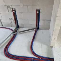 Instalacja rur grzewczych (czerwone i niebieskie) oraz szarych rur kanalizacyjnych w bruzdach w ścianie z betonu komórkowego i na podłodze z izolacją.