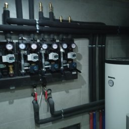 INSTAL AQUA Waldemar Dzierżak - Rozdzielacz ogrzewania podłogowego z manometrami i rurami w Bytomiu. Widoczny również zasobnik ciepłej wody i niebieski zbiornik wyrównawczy.