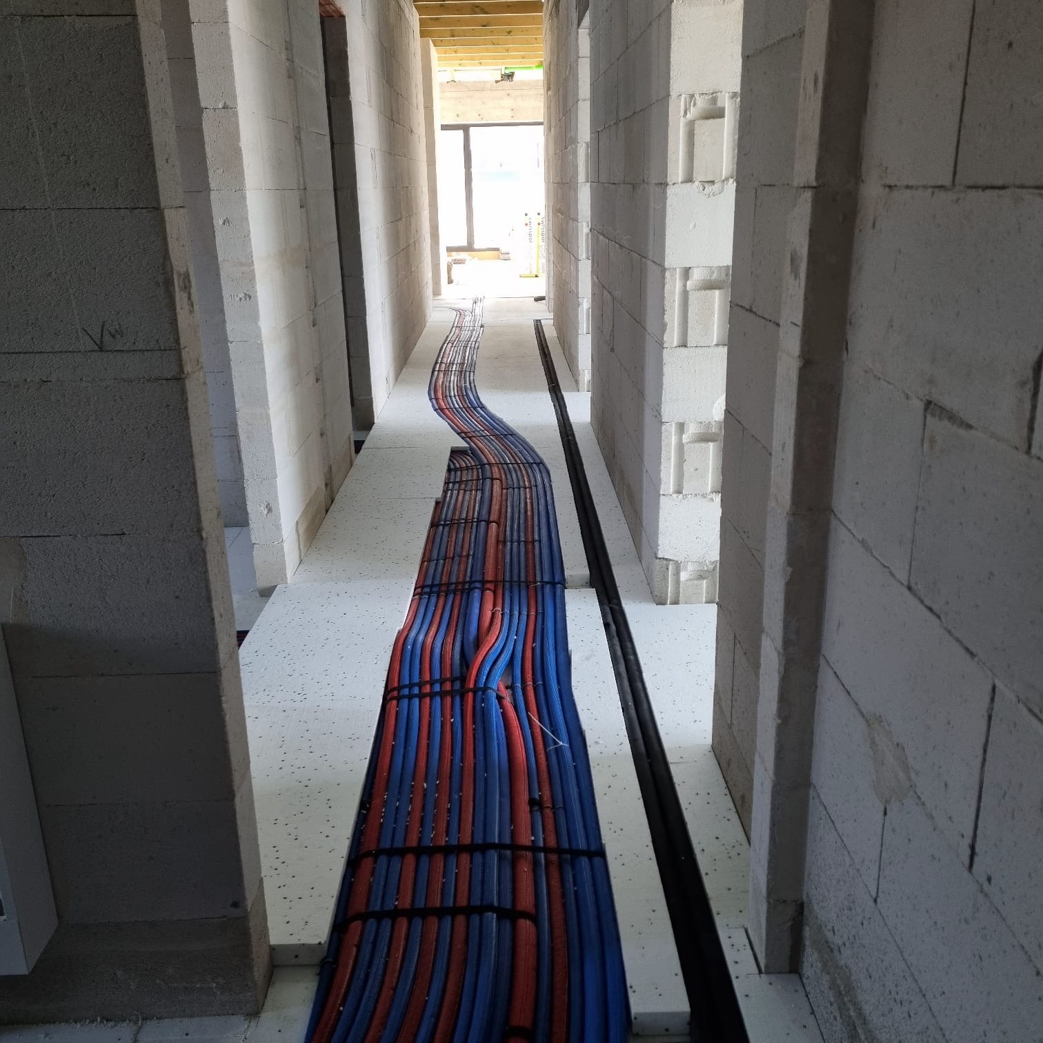 Instalacja rur ogrzewania podłogowego w surowym stanie, widok z góry. Czerwono-niebieskie rury ułożone równolegle między ścianami z betonu komórkowego.