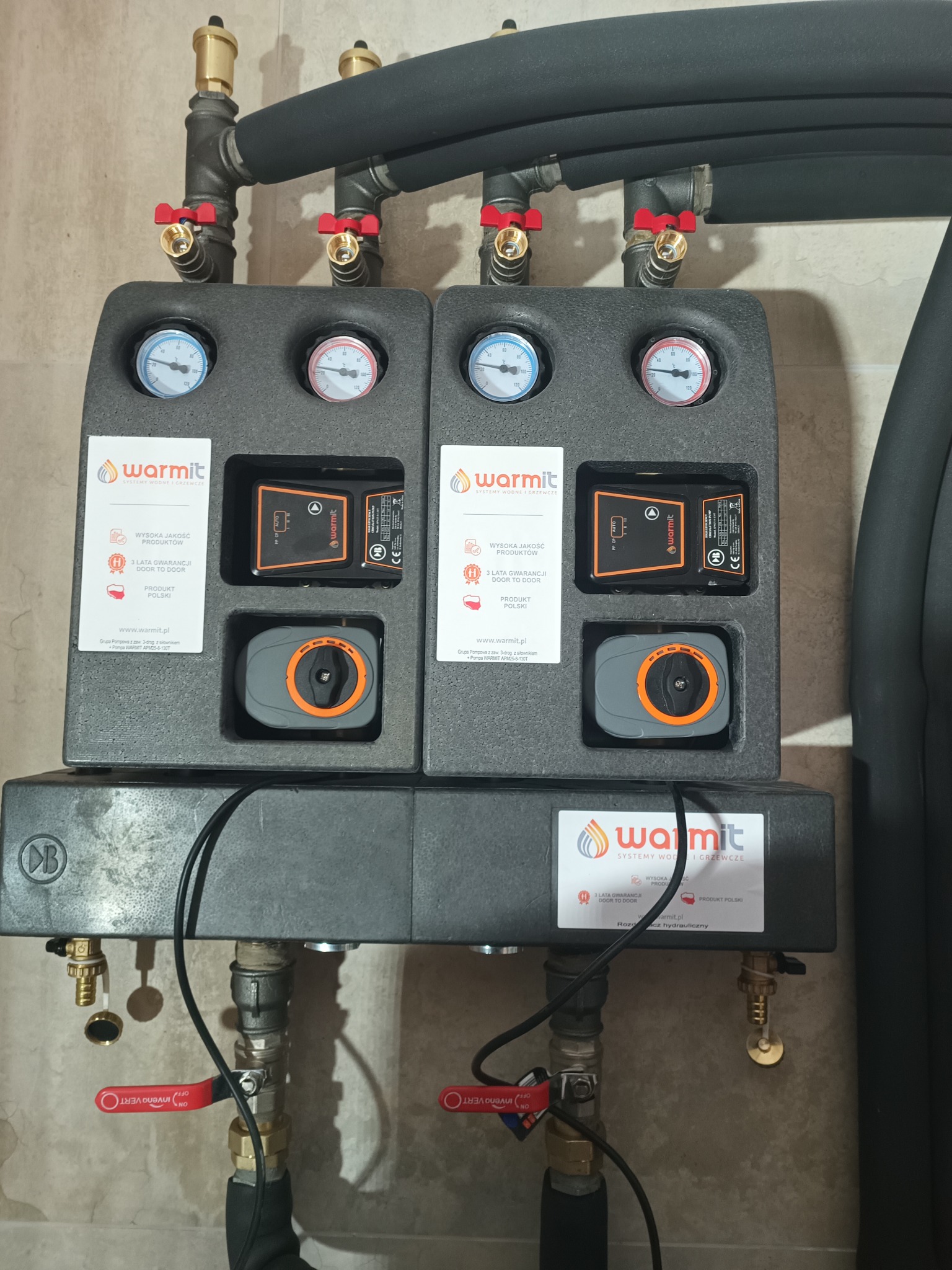 Dwa moduły pompowe WARMIT z manometrami i pompami obiegowymi, zamontowane na ścianie, z podłączonymi rurami w izolacji. Element instalacji grzewczej.
