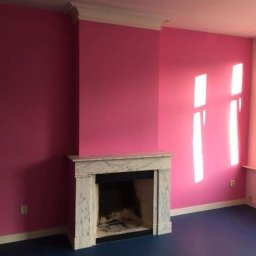 Tommalpol - Pokój z pomalowanymi na różowo ścianami, białym marmurowym kominkiem i ciemnoniebieską podłogą, widoczne światło słoneczne padające przez okno.