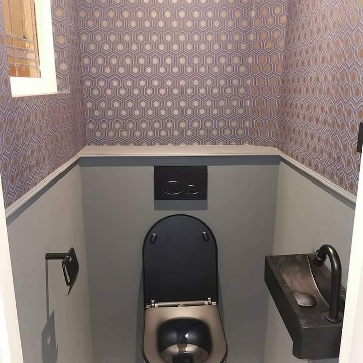 Mała toaleta dla gości z tapetą w geometryczne wzory, szarą farbą na ścianach i czarną armaturą, w tym umywalką i toaletą z podwieszanym systemem spłukiwania.