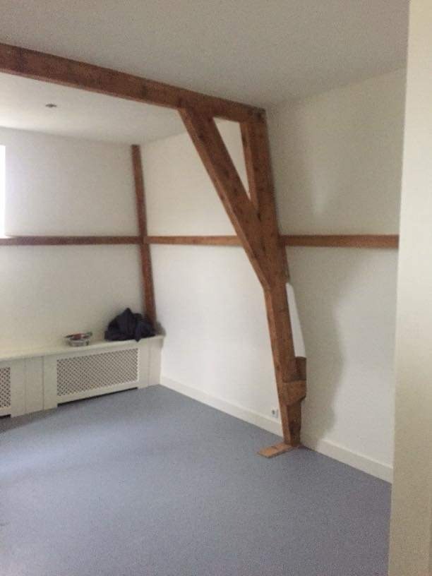 Pusty pokój z szarą podłogą, białymi ścianami i dekoracyjnymi drewnianymi belkami konstrukcyjnymi