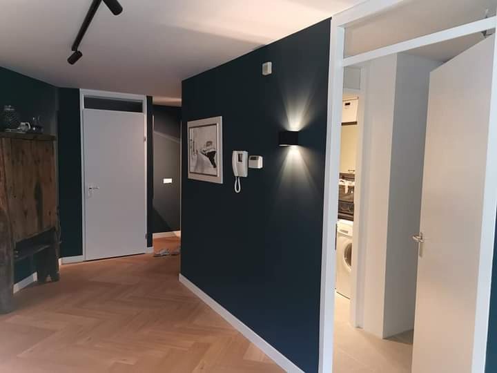 Wnętrze mieszkania po remoncie: ciemne ściany, parkiet ułożony w jodełkę, białe drzwi i ościeżnice, nowoczesne oświetlenie ścienne.