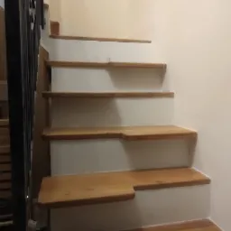 Schody drewniane z białymi podstopnicami i czarną metalową balustradą, widok z dołu, jasne wnętrze.