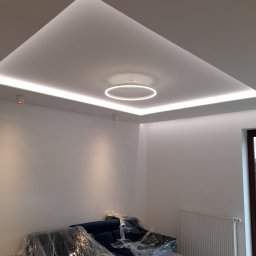 Usługi wykończeniowe - Nowoczesny sufit podwieszany z oświetleniem LED w kształcie kwadratu i okręgu, zabezpieczone meble folią ochronną.