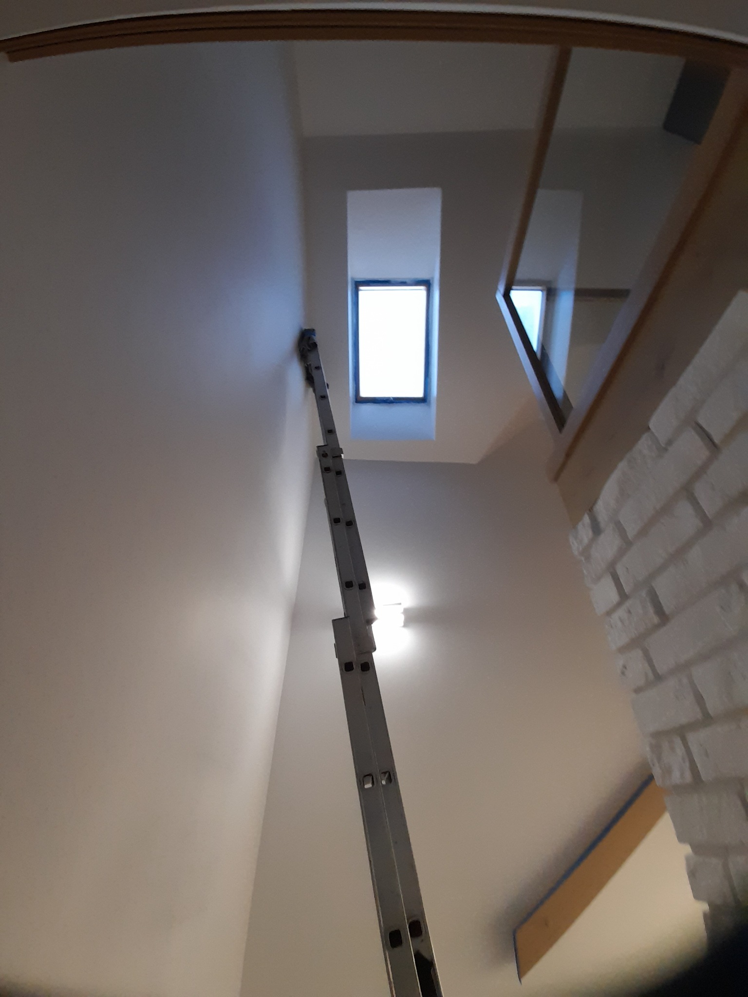 Wnętrze w trakcie odświeżania: rozstawiona drabina teleskopowa pod oknem dachowym, ściana przygotowana do malowania, widoczny fragment ściany z cegły pomalowanej na biało.