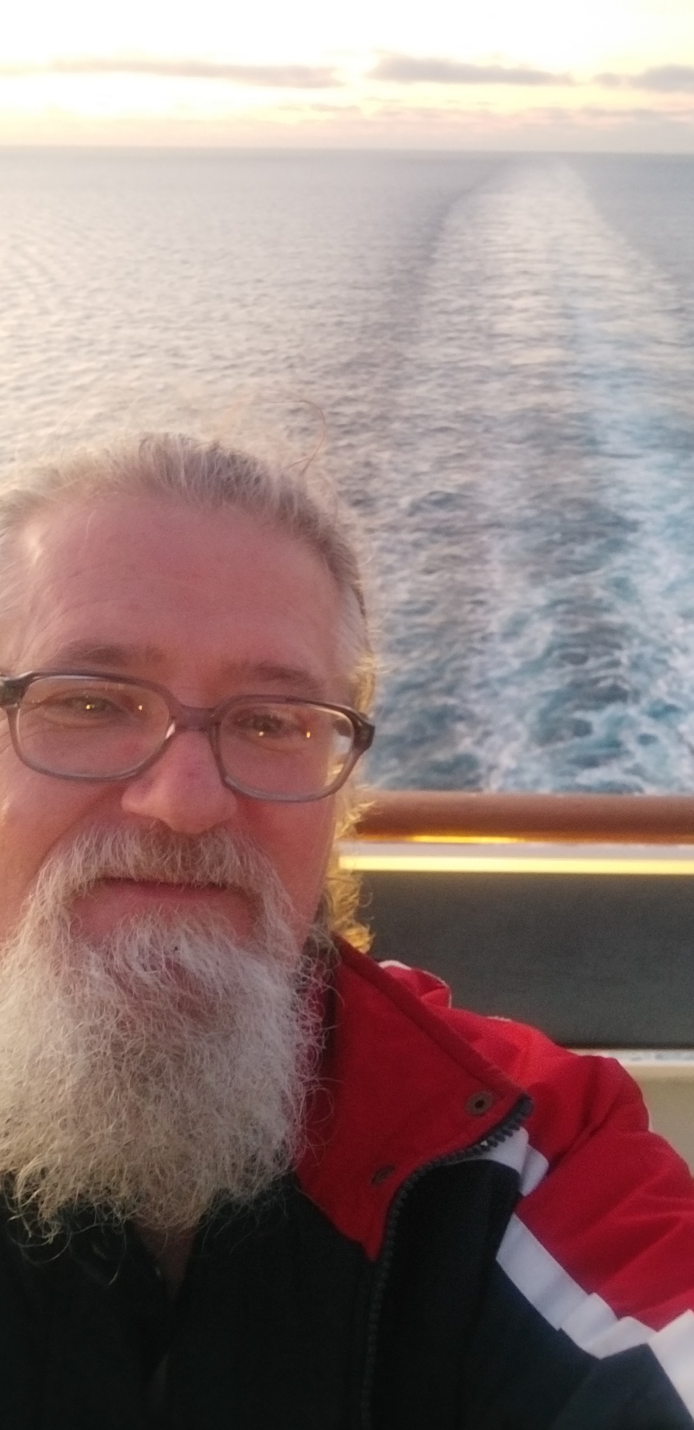 Selfie mężczyzny z brodą na tle morza z widocznym śladem po rejsie statkiem.