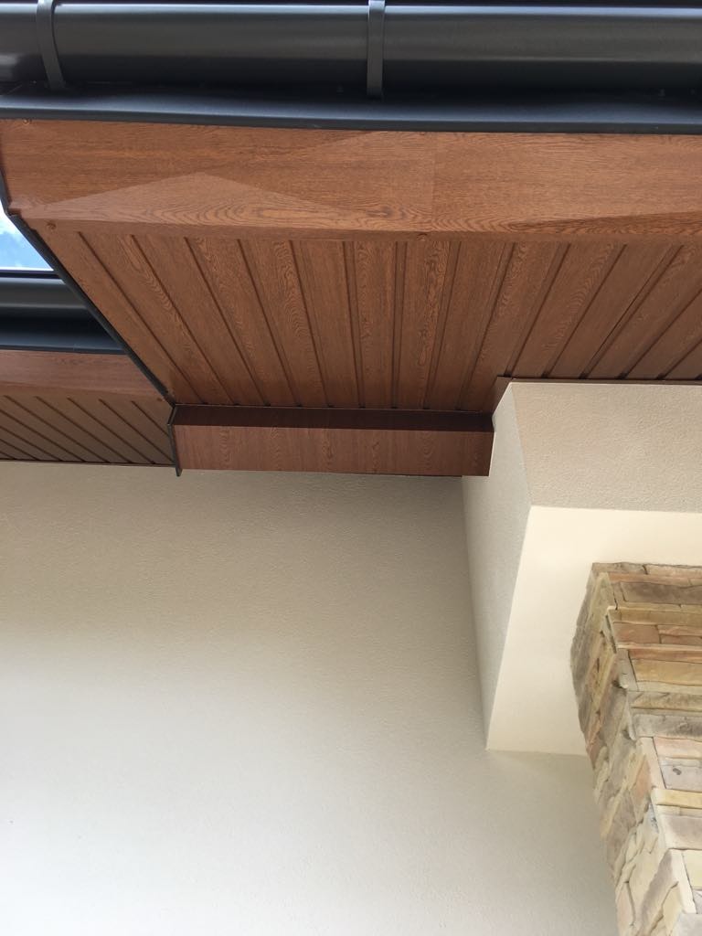 Podbitka dachowa z paneli imitujących drewno, widoczna z dołu, z elementami elewacji wykończonymi kamieniem naturalnym