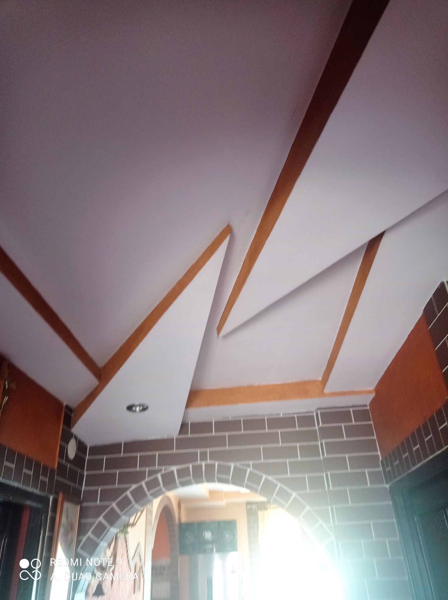 Dekoracyjny sufit z elementami z płyty gipsowo-kartonowej i oświetleniem punktowym, fragment ściany imitującej cegłę, widok z dołu.