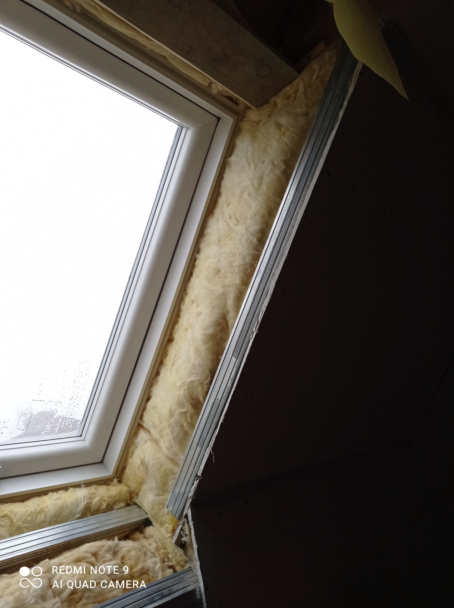 Okno dachowe podczas montażu, ocieplone wełną mineralną i zabezpieczone metalowym profilem w konstrukcji poddasza.