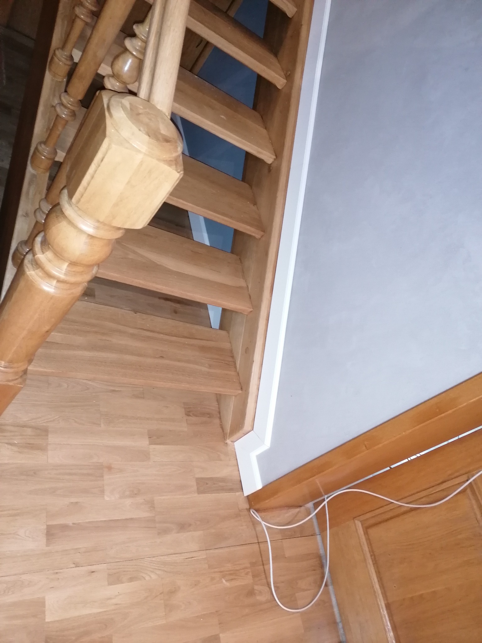 Drewniane schody z toczoną balustradą i panelami podłogowymi w jasnym odcieniu dębu, widok z dołu w kierunku góry, przy białej ścianie.