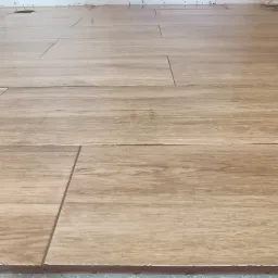 Ułożona podłoga z płytek imitujących drewno, widoczne fugi i pozostałości zaprawy przy ścianie.