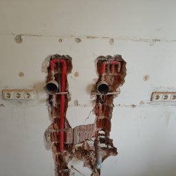 Phu Tomasz Sobieska - Ściana z widocznymi instalacjami hydraulicznymi w trakcie prac remontowych, z odsłoniętą cegłą i gniazdkami elektrycznymi.