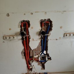 Phu Tomasz Sobieska - Ściana z odsłoniętymi rurami (czerwone i niebieskie) w dwóch miejscach, widoczne gniazdka elektryczne i gruz na podłodze. Etap prac instalacyjnych wewnątrz budynku.