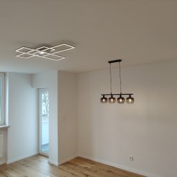 Phu Tomasz Sobieska - Jasne, przestronne wnętrze po odnowieniu w Wolnzach: parkiet, białe ściany, nowoczesne lampy sufitowe i okno z widokiem na miasto. Minimalistyczny design.