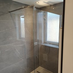 Phu Tomasz Sobieska - Nowoczesna kabina prysznicowa z szarymi płytkami imitującymi marmur i odpływem liniowym, widok z zewnątrz. W tle okno z mleczną szybą.