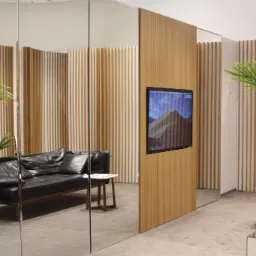 Nowoczesne wnętrze biurowe z czarną skórzaną sofą, rośliną w lustrzanej donicy i panelem z wbudowanym ekranem wyświetlającym górski krajobraz.