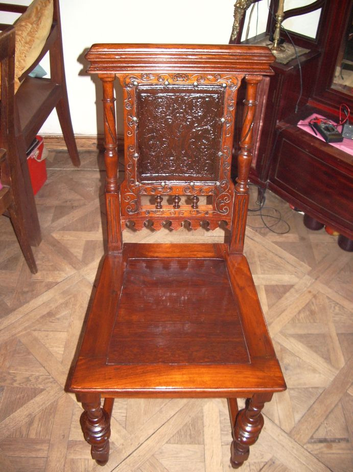 Antyczne, drewniane krzesło z rzeźbionym oparciem i siedziskiem, odnowione z widoczną politurą, stoi na parkiecie.