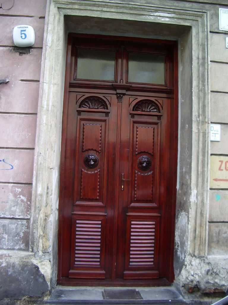 Odrestaurowane, dwuskrzydłowe, drewniane drzwi wejściowe w kamienicy, z dekoracyjnymi rzeźbieniami lwów i numerem budynku 'Targowa 5'.