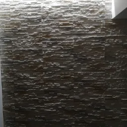 Ściana wyłożona dekoracyjnym kamieniem w odcieniach szarości, oświetlona od góry listwą LED, tworząca efekt trójwymiarowej tekstury.