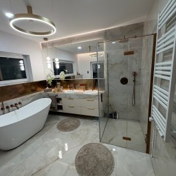 Solid Bud - Elegancka łazienka z wanną wolnostojącą, kabiną prysznicową ze szklanymi drzwiami i marmurowymi płytkami. Złote akcenty armatury i oświetlenia dodają luksusowego charakteru.