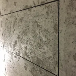 Szare, matowe płytki imitujące beton z ciemnymi fugami, ułożone na ścianie pod kątem.