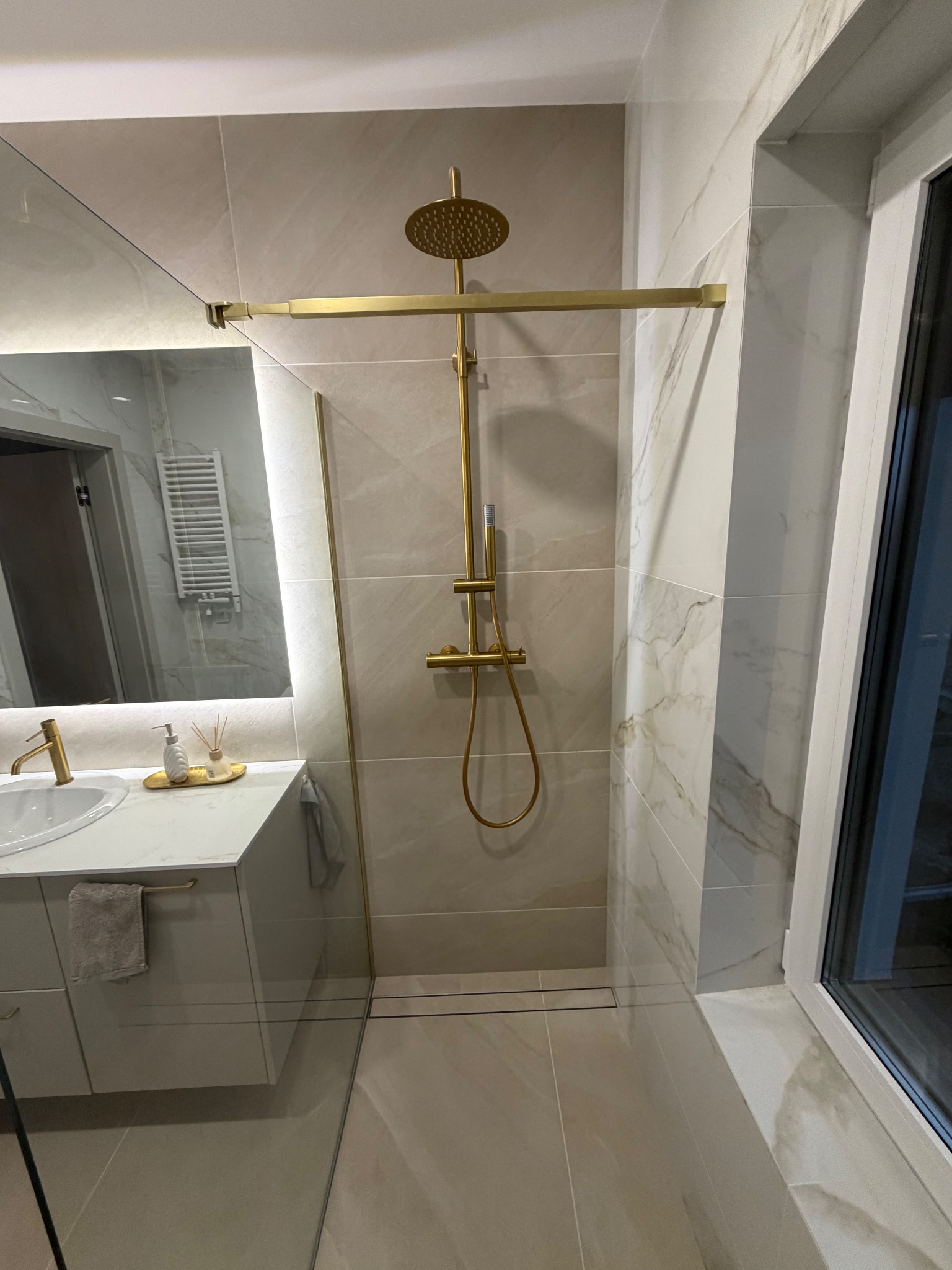 Stylowa kabina prysznicowa z złotą armaturą i odpływem liniowym, wykończona płytkami imitującymi marmur w Lublińcu. Nowoczesny design i dbałość o detale.