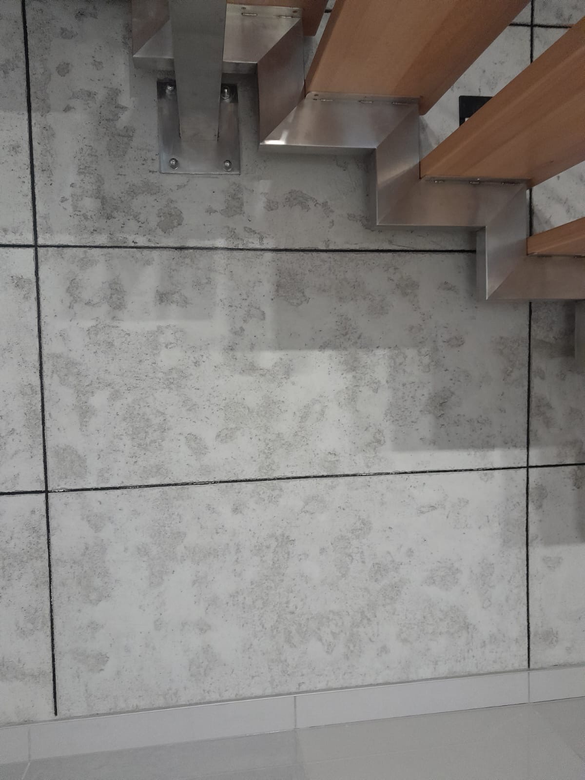 Ściana wykończona płytami imitującymi beton, z widocznymi metalowymi elementami konstrukcji schodów z drewnianymi stopniami.