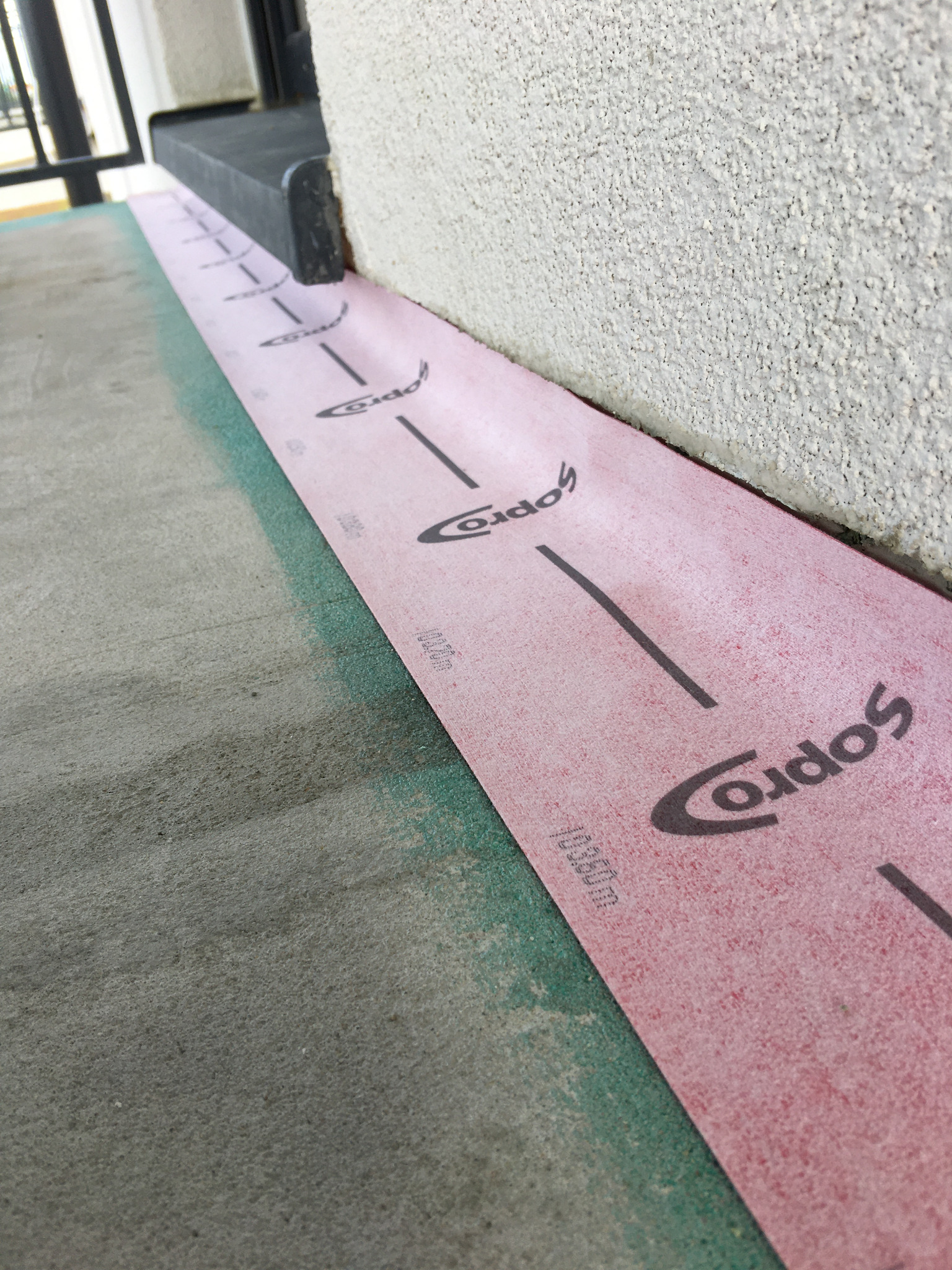 Przygotowanie podłoża pod wylewkę z użyciem różowej membrany izolacyjnej z nadrukowaną miarką, widoczne połączenie ściany z podłożem.