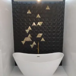 Nowoczesna łazienka z wolnostojącą białą wanną na tle ściany z czarnych trójwymiarowych płytek z geometrycznym wzorem złotych trójkątów, oświetlona pojedynczą żarówką.