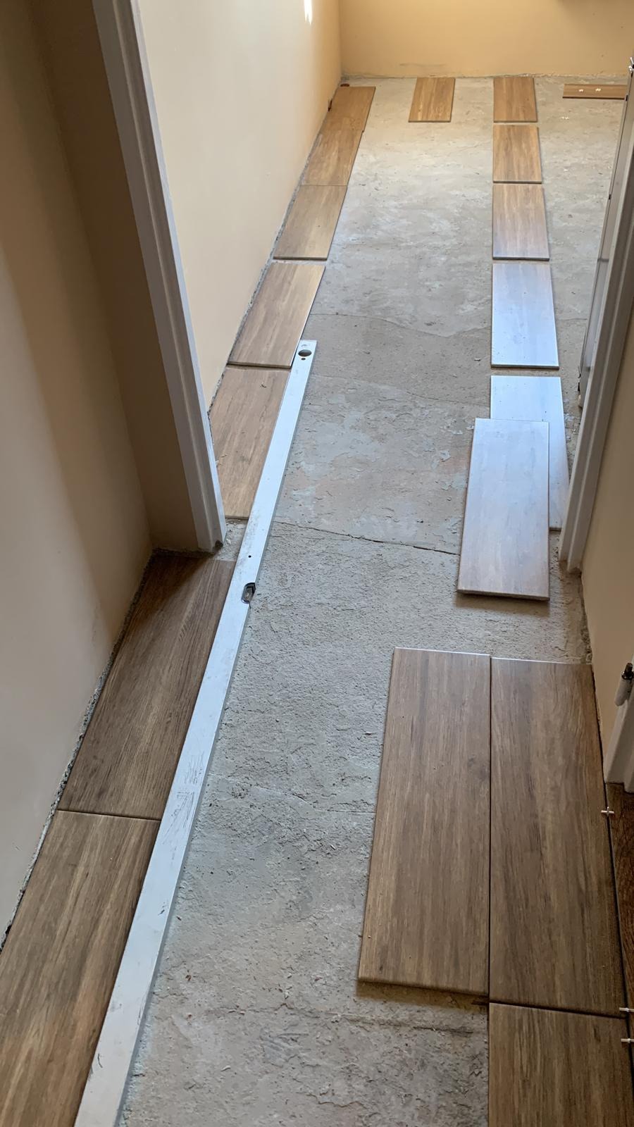 Układanie podłogi z płytek imitujących drewno w wąskim korytarzu, widoczny poziomica i częściowo ułożone płytki w dwóch odcieniach brązu na szarym podłożu.