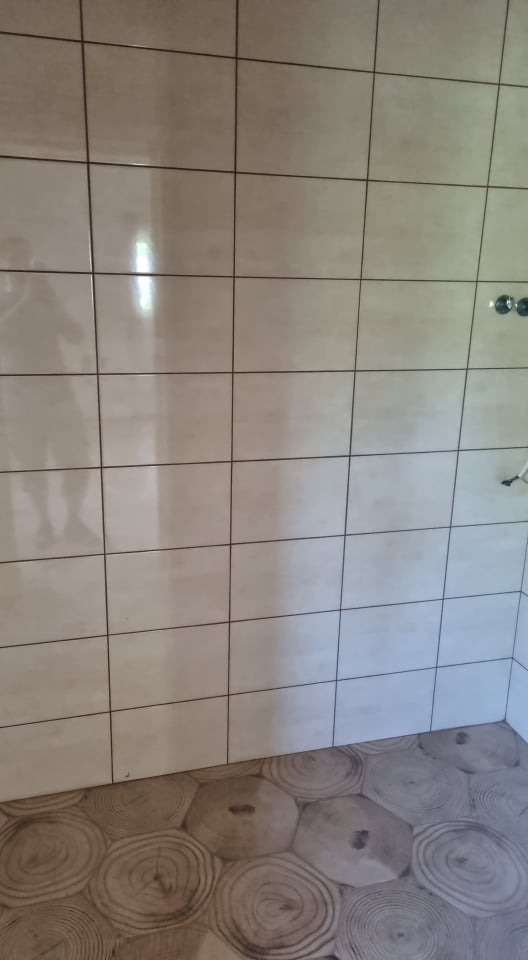 Wykończona ściana w łazience w Pakości z jasnymi płytkami ceramicznymi i podłogą imitującą przekrój drewna.