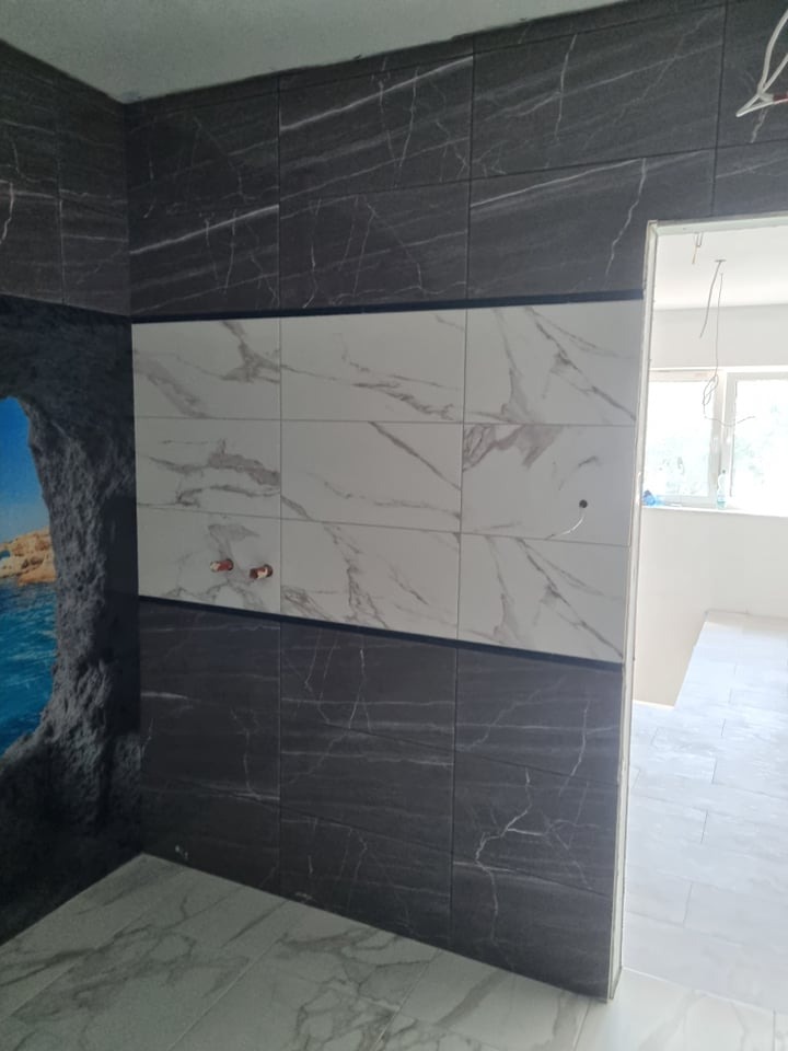 Częściowo wykończona łazienka z czarno-białymi płytkami imitującymi marmur, z widoczną instalacją wodną i fototapetą z motywem morskim.