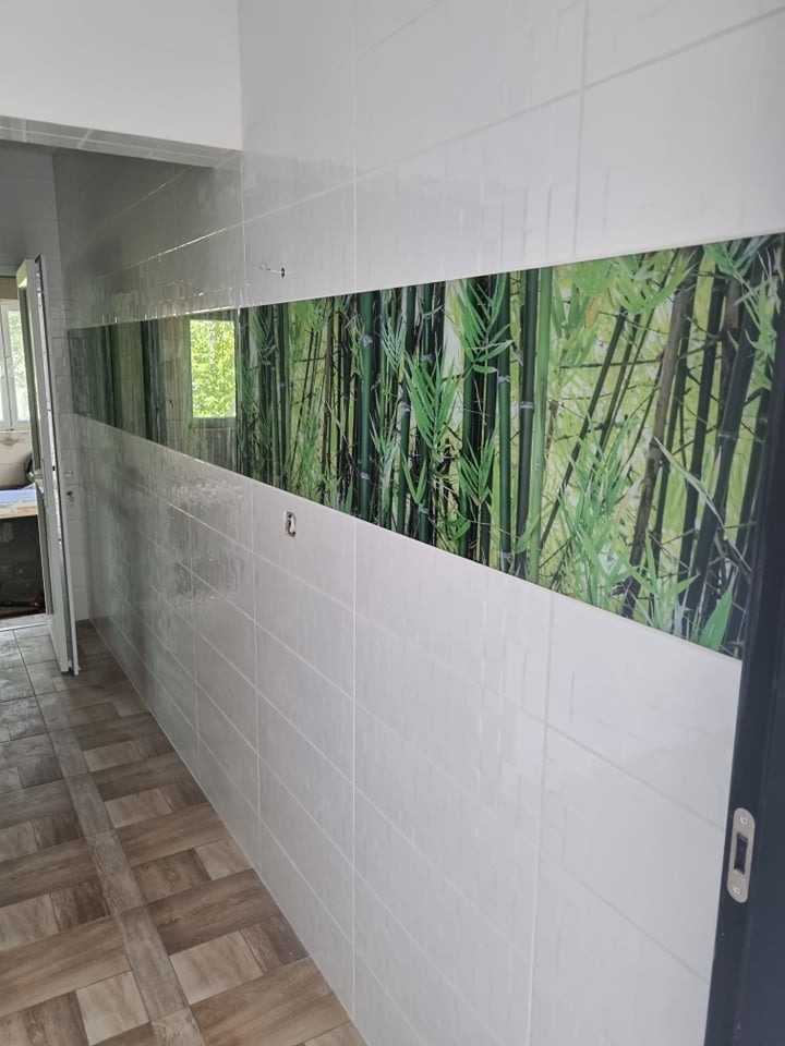 Korytarz wyłożony białymi, prostokątnymi płytkami z poziomym pasem dekoracyjnym z motywem bambusowego lasu; podłoga wyłożona płytkami imitującymi drewno; widoczne drzwi i okno.