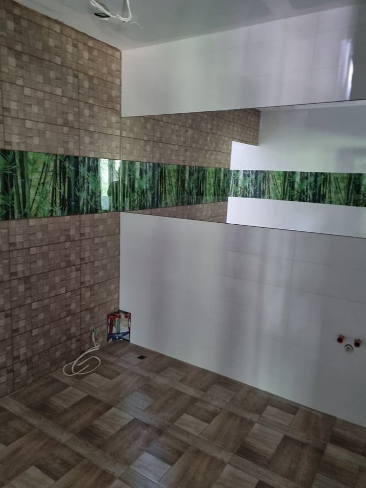 Wnętrze kuchni w trakcie wykańczania, z brązowymi płytkami imitującymi cegłę, pasem dekoracyjnym z motywem bambusa i białymi, błyszczącymi płytkami, widoczne przewody elektryczne i otwarte...