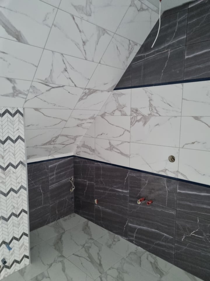 Fragment wykończonej łazienki z białymi i grafitowymi płytkami imitującymi marmur na ścianach oraz podłodze, z dekoracyjnym pasem płytek w zygzaki.