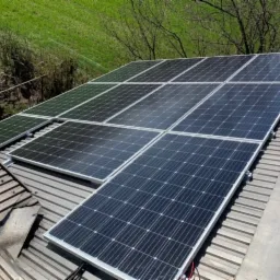 Panel słoneczny na metalowym dachu z widoczną zielenią w tle, montaż ukończony.