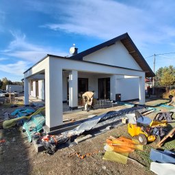 LUK-BUD Łukasz Wołoch - Biały budynek z kolumnami w trakcie wykończenia elewacji, widoczne narzędzia i materiały budowlane, błękitne niebo w tle. Prace wykończeniowe.