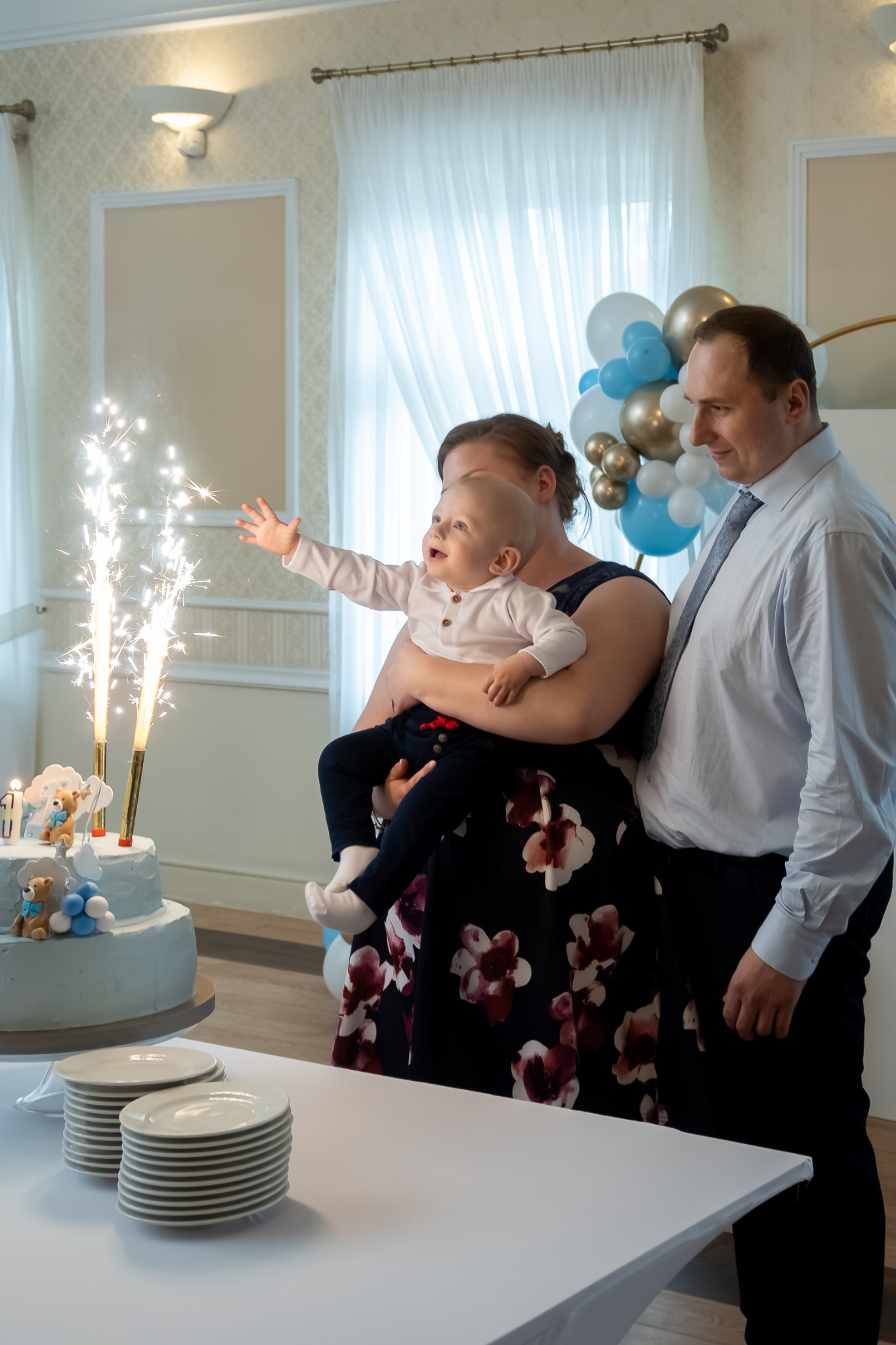 Rodzina świętuje pierwsze urodziny dziecka z tortem i fontannami iskier w eleganckim wnętrzu.