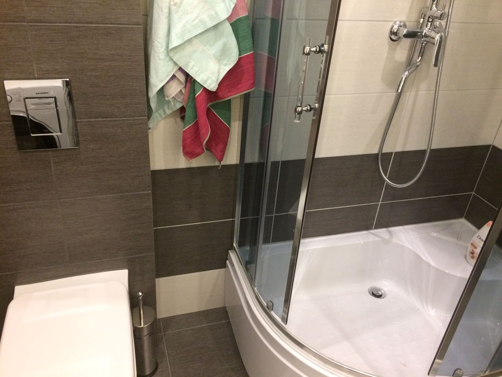 Nowoczesna łazienka z kabiną prysznicową z zaokrąglonym narożnikiem, wiszącą toaletą i szarymi płytkami ułożonymi w poziome pasy.